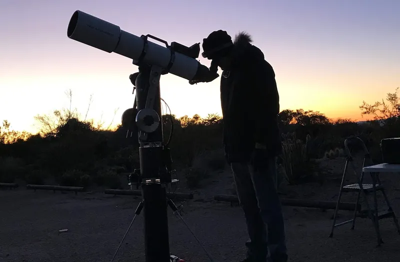 An attendee looking through a refractor telescope at sunset in the desert