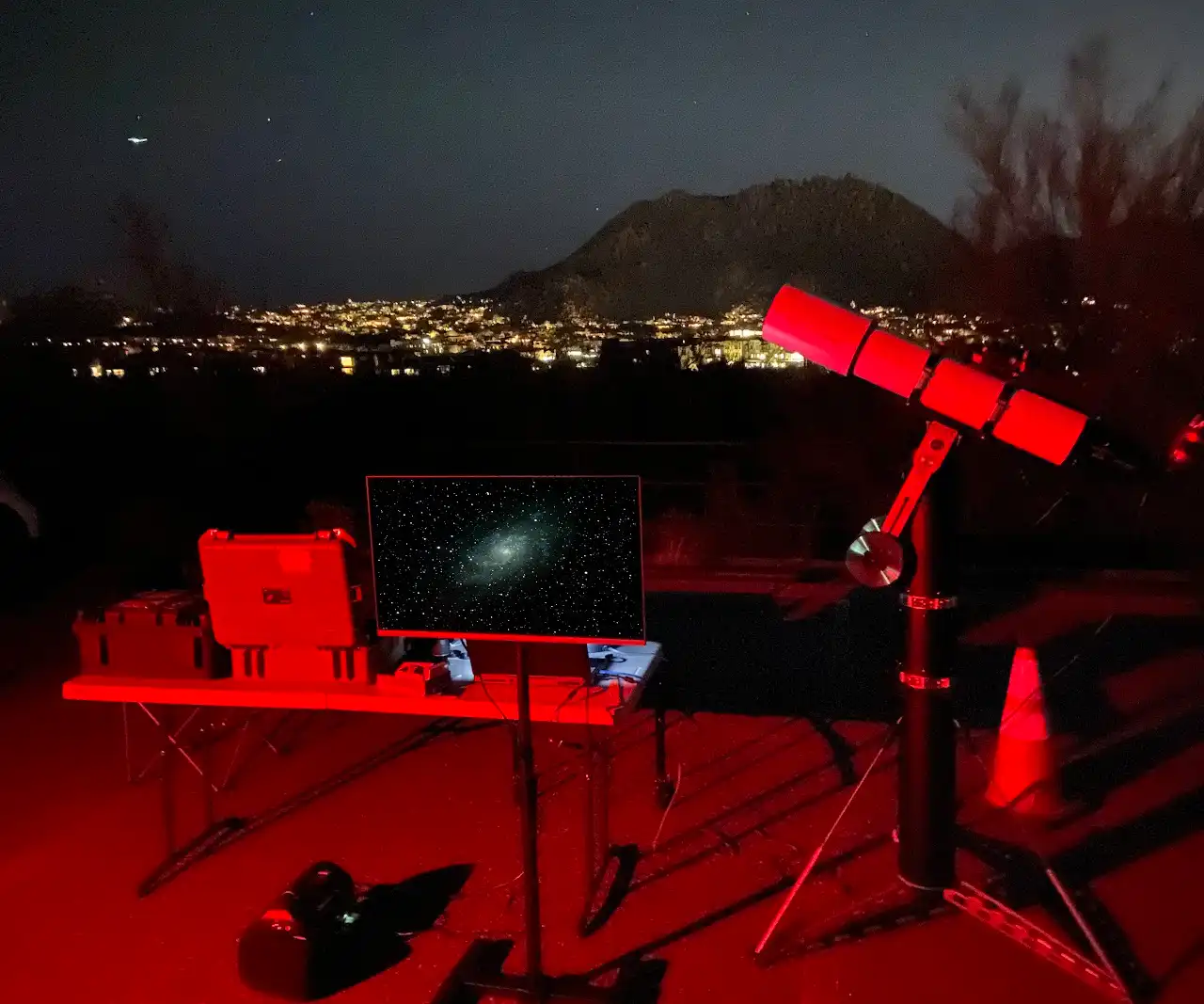 A PAS electronically-assisted-astronomy rig under the night sky, lit red, with city lights on the horizon
