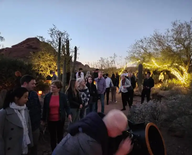 PAS members and guests gathered around a telescope at dusk, with string lights and desert cactus around them
